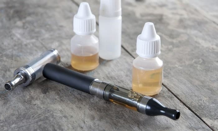 Two e-cigarette devices and several small bottles of liquid nicotine on a wooden surface.