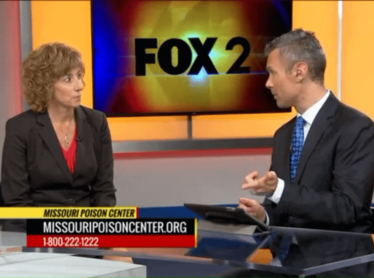A Missouri Poison Center representative being interviewed by a Fox 2 news anchor on set, with a lower-third graphic displaying 'Missouri Poison Center — missouripoisoncenter.org — 1-800-222-1222.'