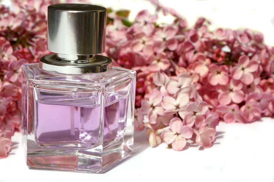 A perfume bottle in front of lilac flowers.