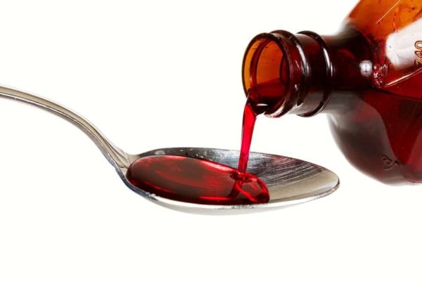 Cough syrup being poured from a brown bottle onto a spoon
