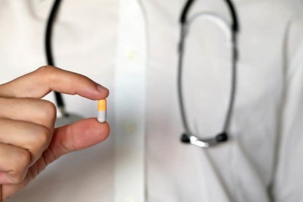 A doctor holding a white and tan capsule pill between his fingers.
