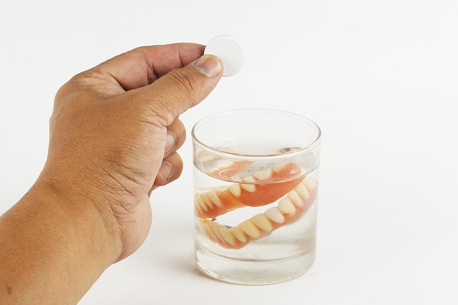 someone with dentures in a glass about to add denture cleansers