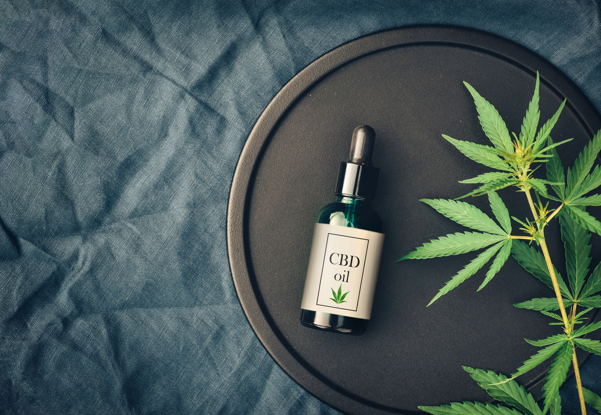 A bottle of CBD oil on a black tray with marijuana leaves around it.