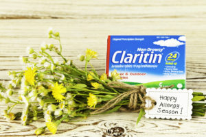 A package of ClaritinⓇ loratadine sits behind a bundle of wildflowers with a card beside the flowers reading “Happy Allergy Season!”