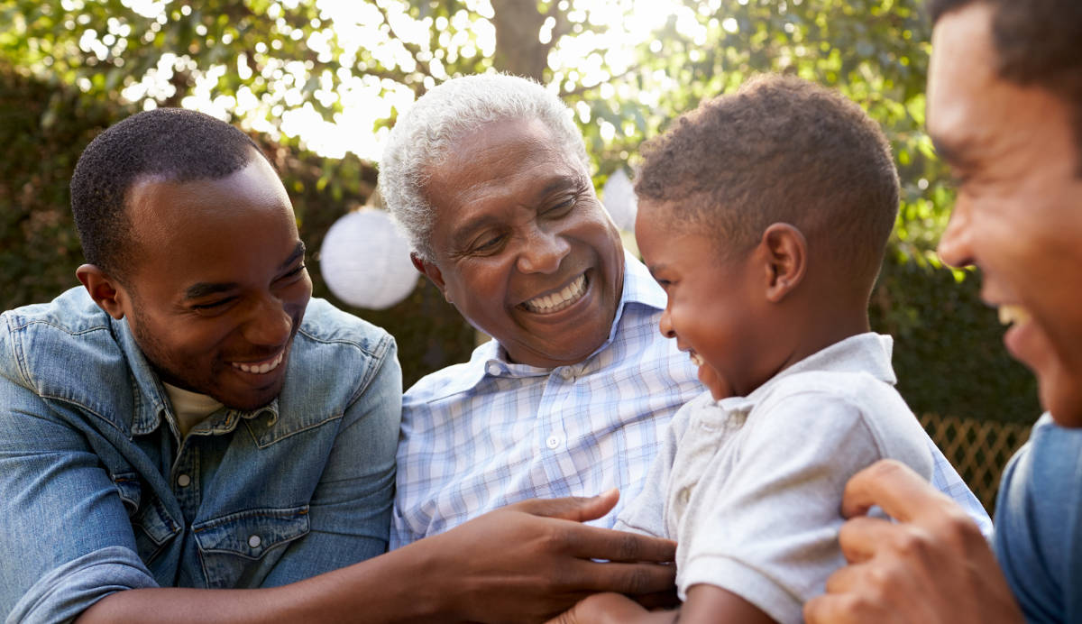 Multi-generational family laughing together outdoors, including a grandfather, adult men, and a young child