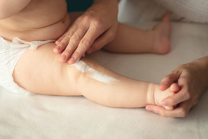 A parent applying baby lotion to their baby's leg.
