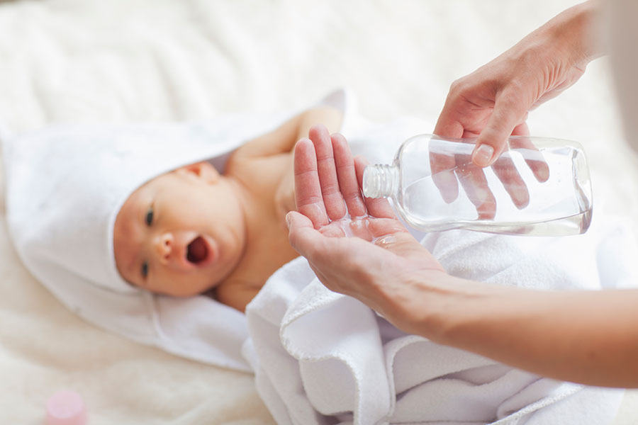 A parent puts baby oil on their hands besides their infant.