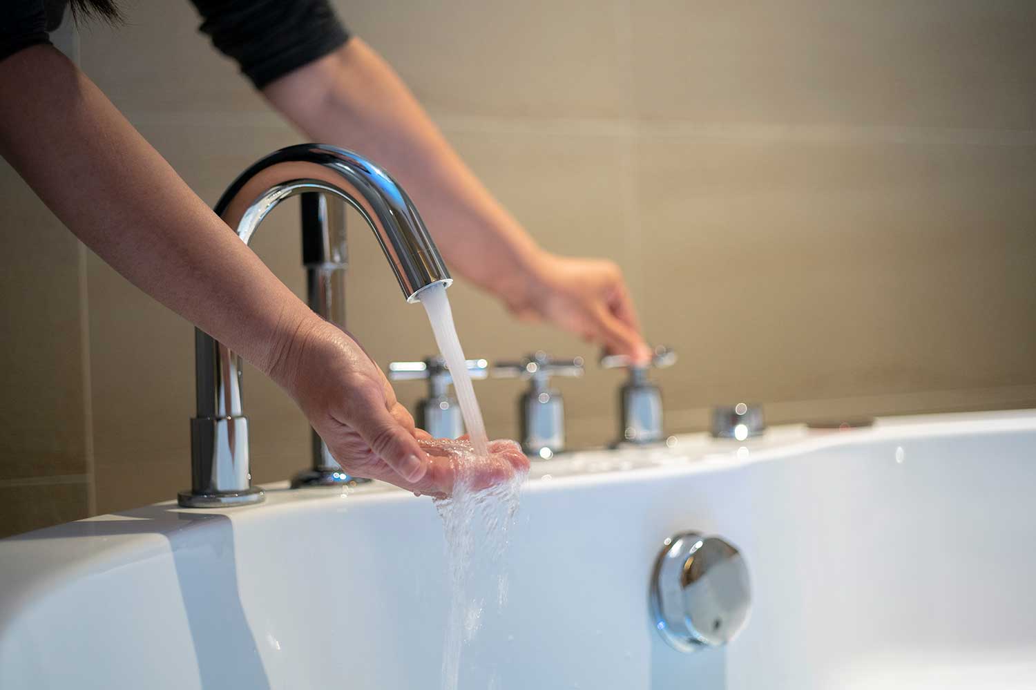 person running hand under bath water faucet