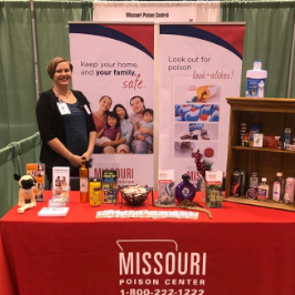 Missouri Poison Center staff member standing at an outreach display table with educational materials and banners
