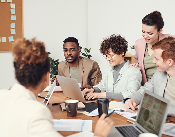 A group of adults collaborating around a table with laptops in an office setting.