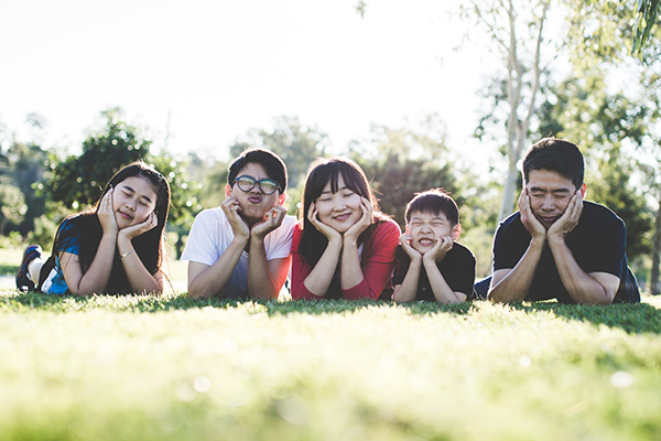 A family of five lying on grass outdoors, smiling with their chins resting in their hands.