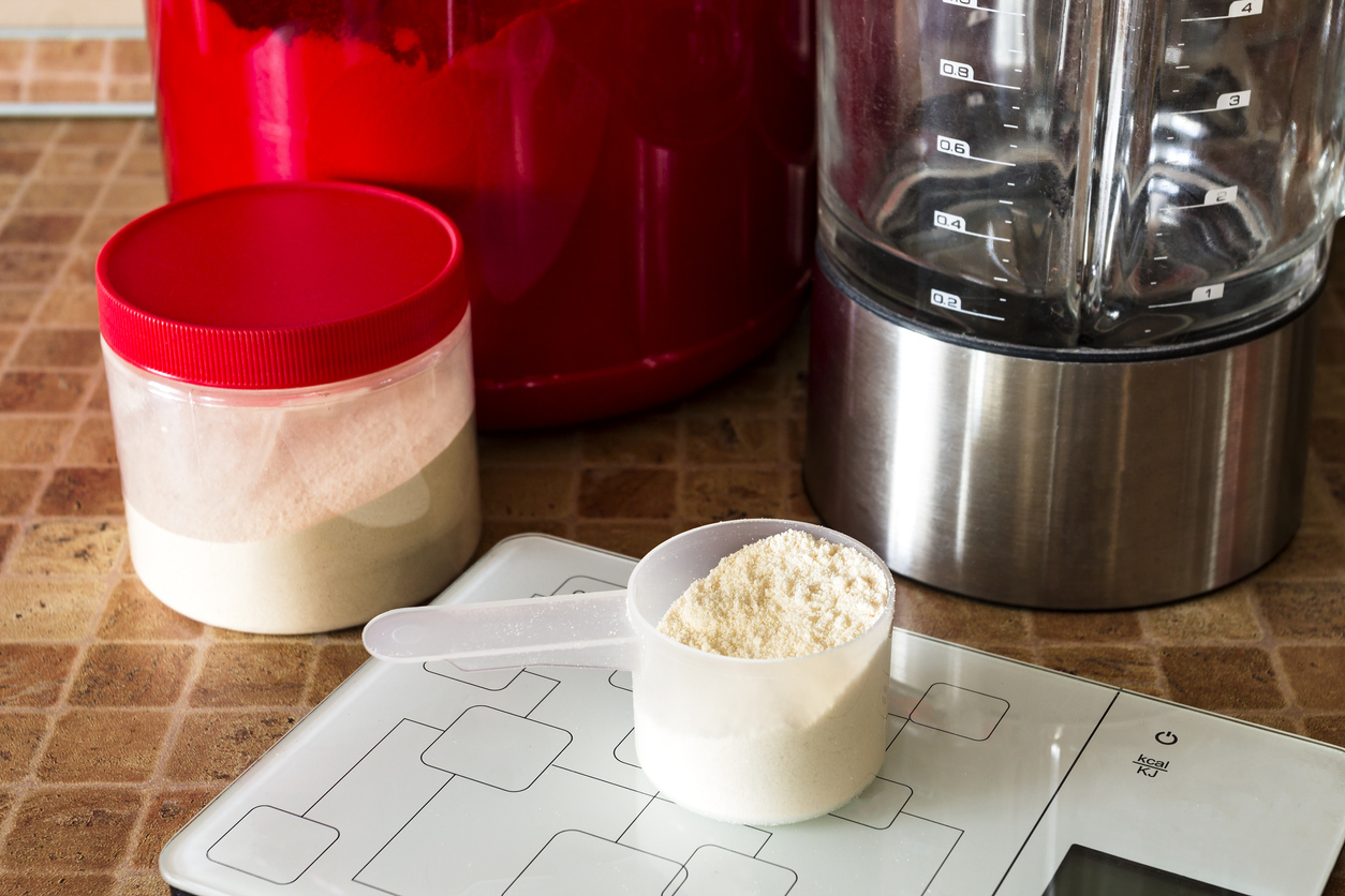 A cup of dry pre-workout powder sitting on a scale besides a blender.