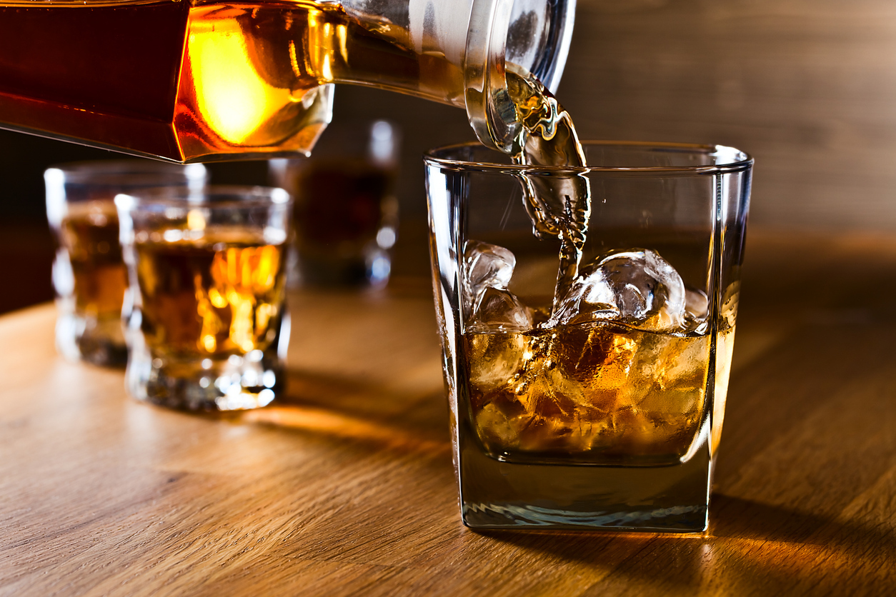 A bartender pouring a glass of whiskey over ice cubes.