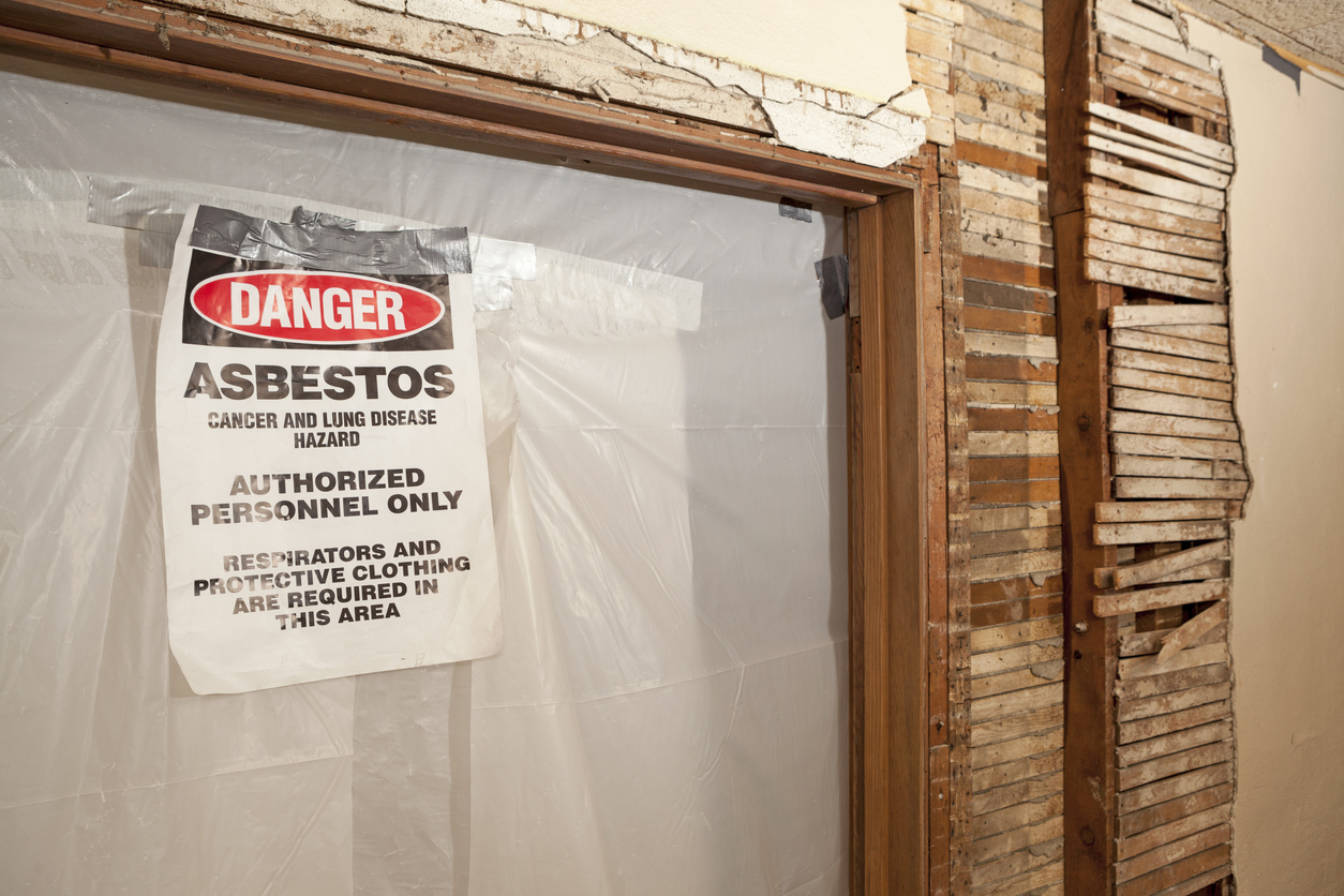 A danger sign posted on a plastic-sheeted doorway in a building under renovation reading 'Danger — Asbestos — Cancer and Lung Disease Hazard — Authorized Personnel Only — Respirators and Protective Clothing Are Required in This Area.'