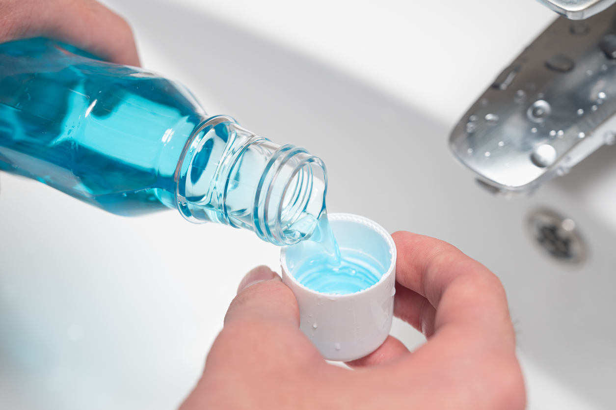 A man poring blue mouth wash with carbamide peroxide into the cap over a sink.