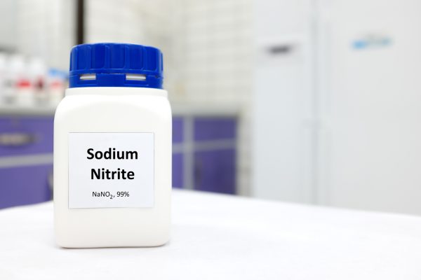 A white laboratory container labeled 'Sodium Nitrite, NaNO2, 99%' with a blue cap.