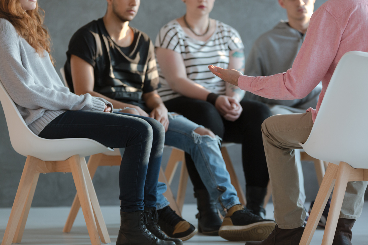 A group of teenagers sitting in a circle during a counseling or support group session with an adult facilitator.