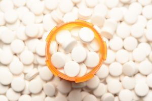 An open orange prescription bottle surrounded by loose white pills