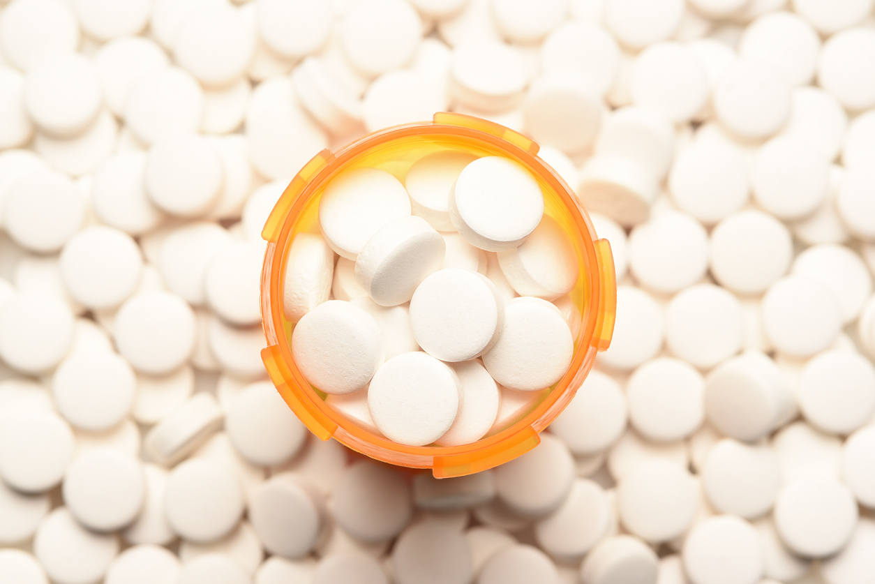 An open orange prescription bottle surrounded by loose white pills