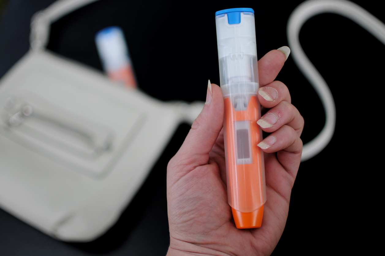 Hand holding an epinephrine auto-injector with a carry case in the background