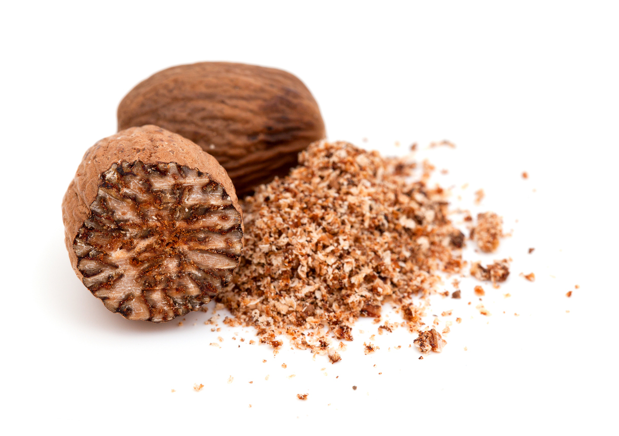 Whole and halved nutmeg seeds next to a pile of ground nutmeg