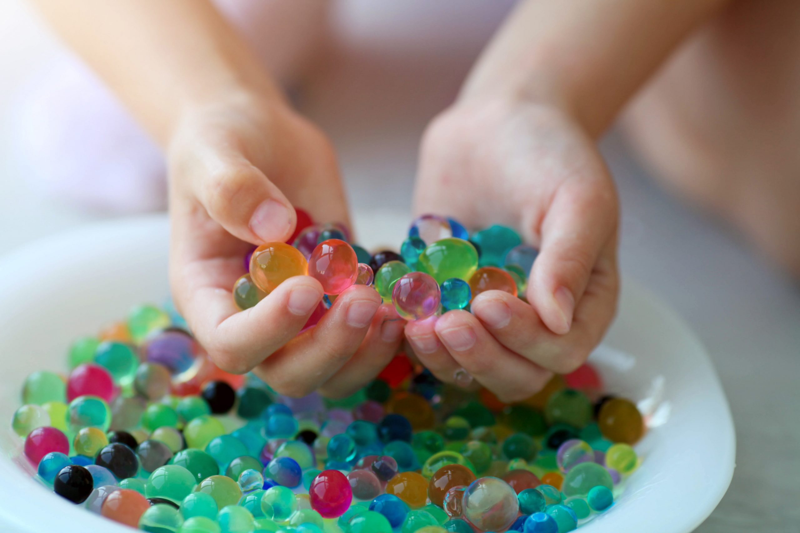 Person's hands scooping colorful water beads from a bowl