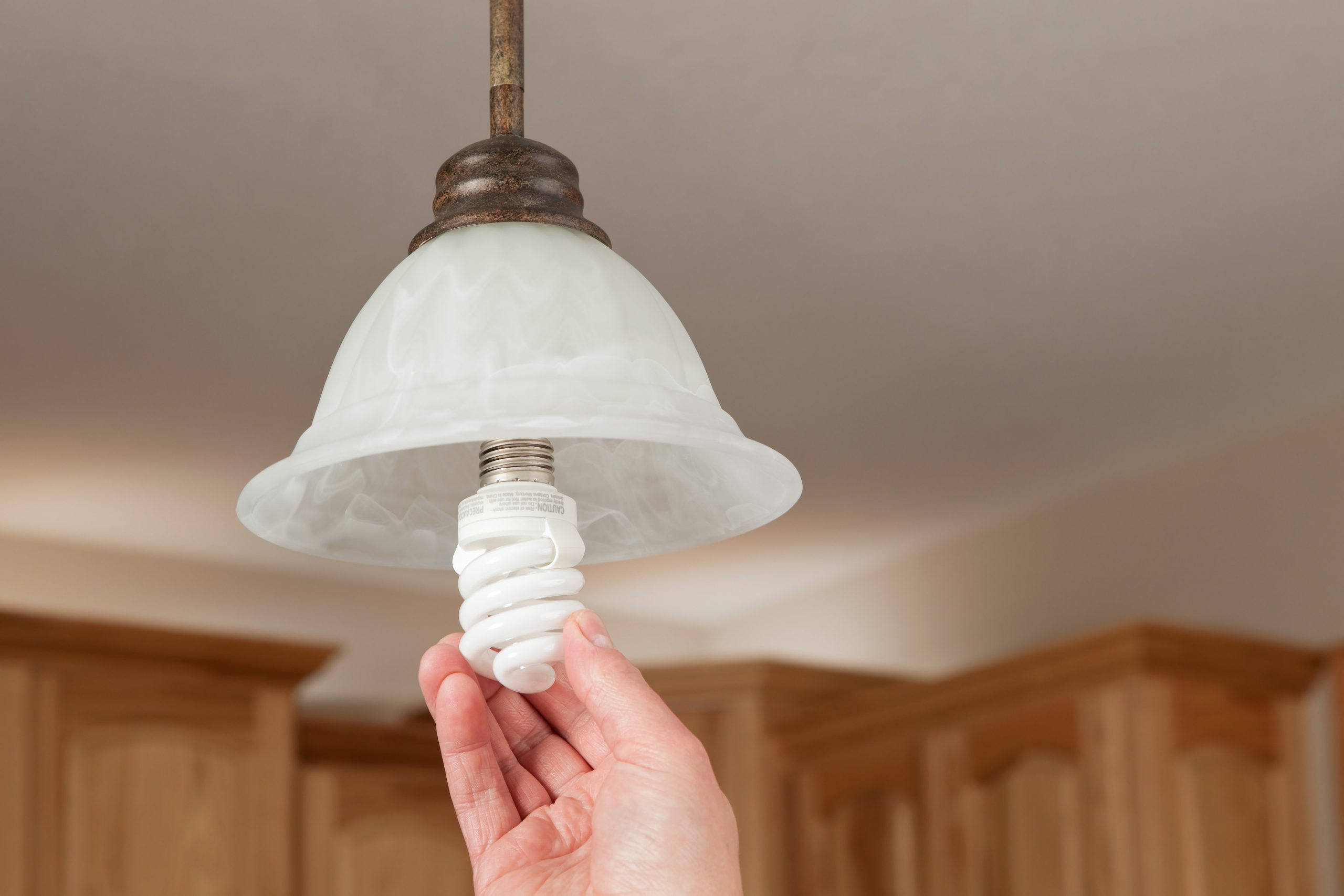 A hand is installing an energy efficient compact fluorescent light bulb (CFL) into a ceiling fixture. 