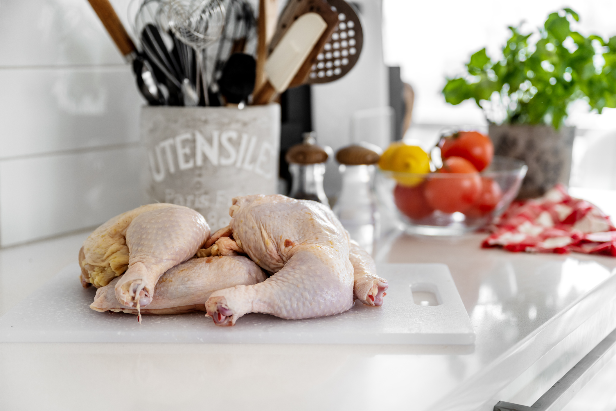 Raw chicken thighs sit on a cutting board on a counter besides tomatoes to represent how uncooked meat can become spoiled food.
