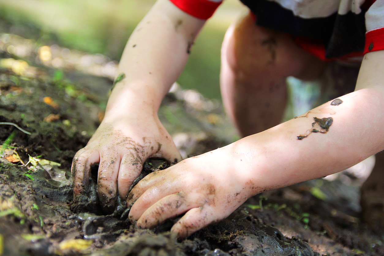 A little boy digging in the dirt with his hands.