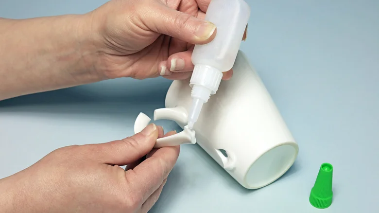 Hands applying super glue to a broken white ceramic mug