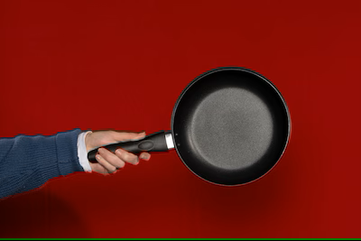 Hand holding a nonstick frying pan against a red background