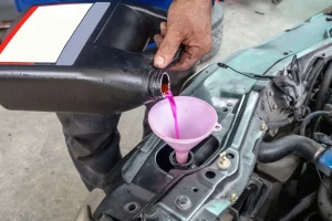 A mechanic pours pink antifreeze into a car.