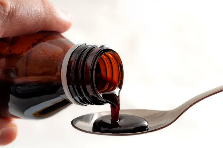 Medicine in syrup form is poured into a spoon.
