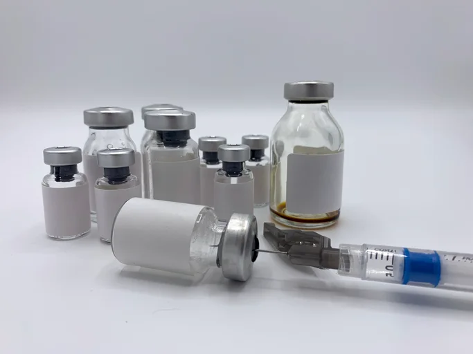 Vials of injectable peptides on a table. A syringe lays on its side.
